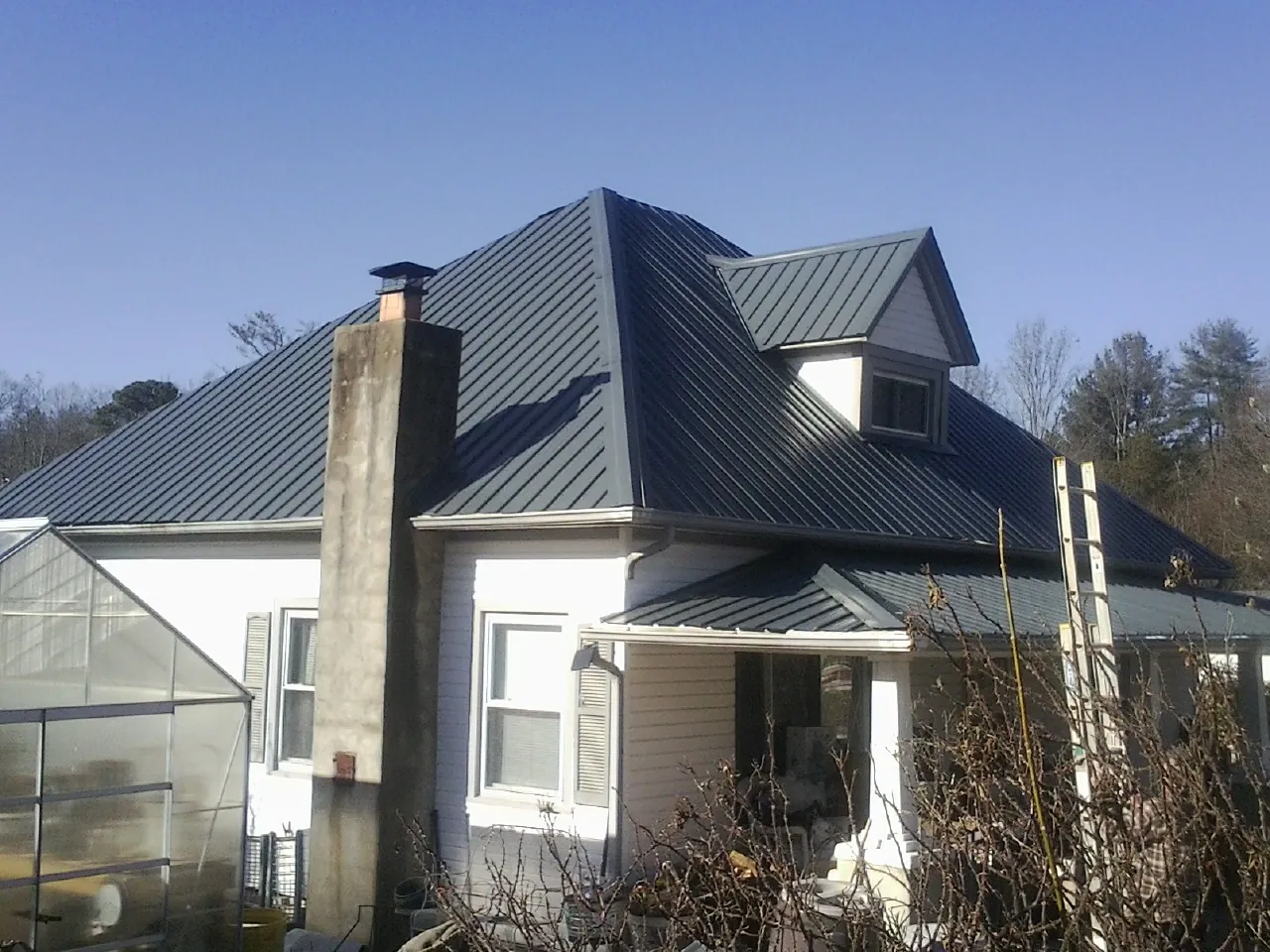 Dark blue standing seam metal roof on a white farmhouse with dormer — Slate & Tile Roof Repair by Roofing Brothers in Quogue