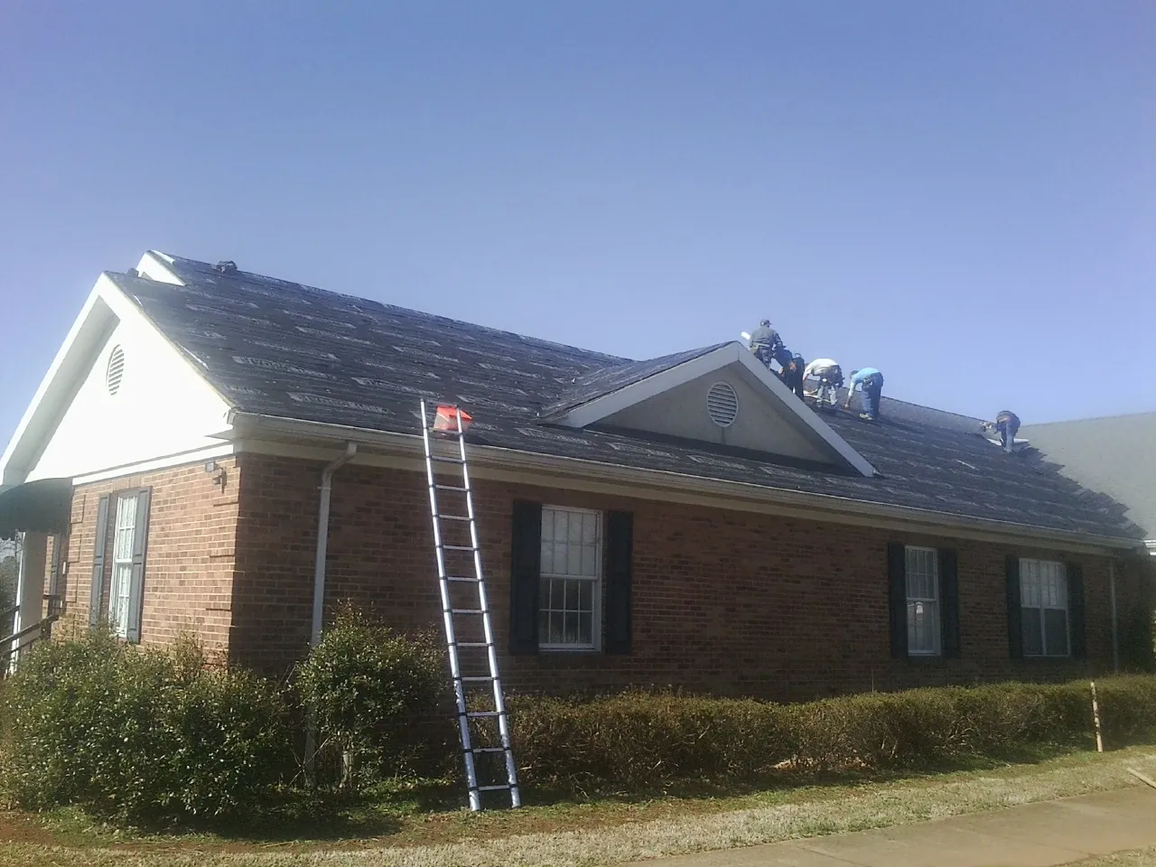Crew tearing shingles off a brick ranch roof with a ladder set — Metal Roof Repair work by our crew in Quogue