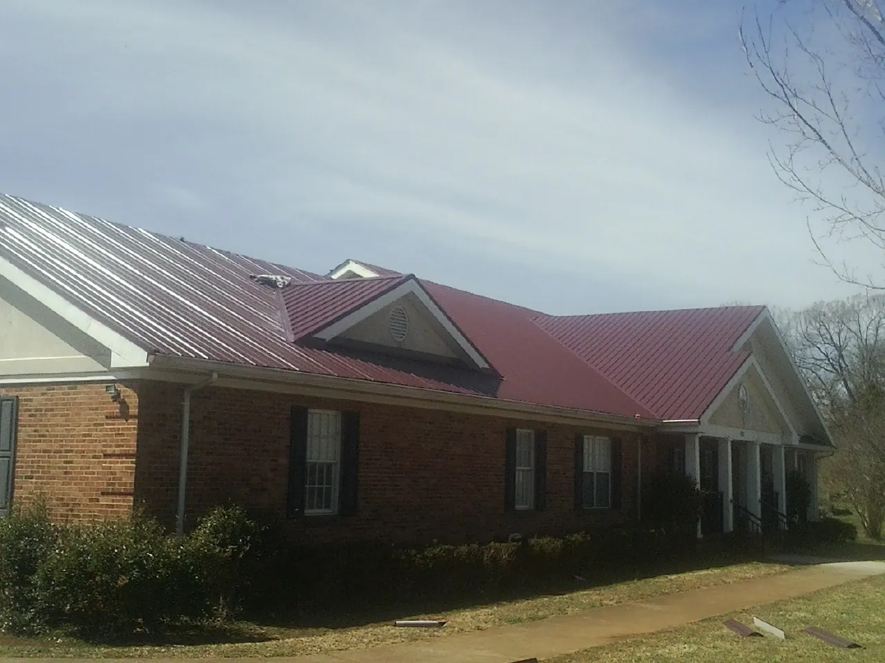 Red metal roof with gabled entries on a long brick building, from a Hail Damage Roof Repair job in Quogue