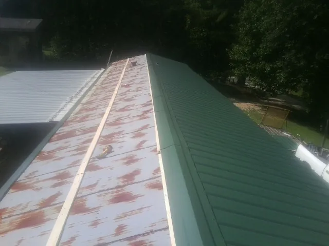 Old rusted panels beside newly installed green metal roofing in Quogue