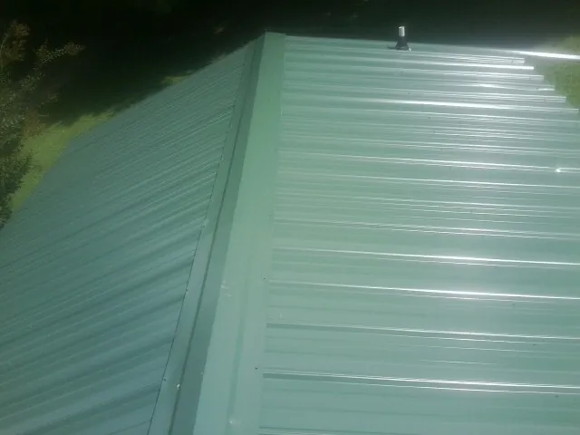 New green metal panels meeting at the ridge of a roof — Flat Roof Repair work by our crew in Quogue