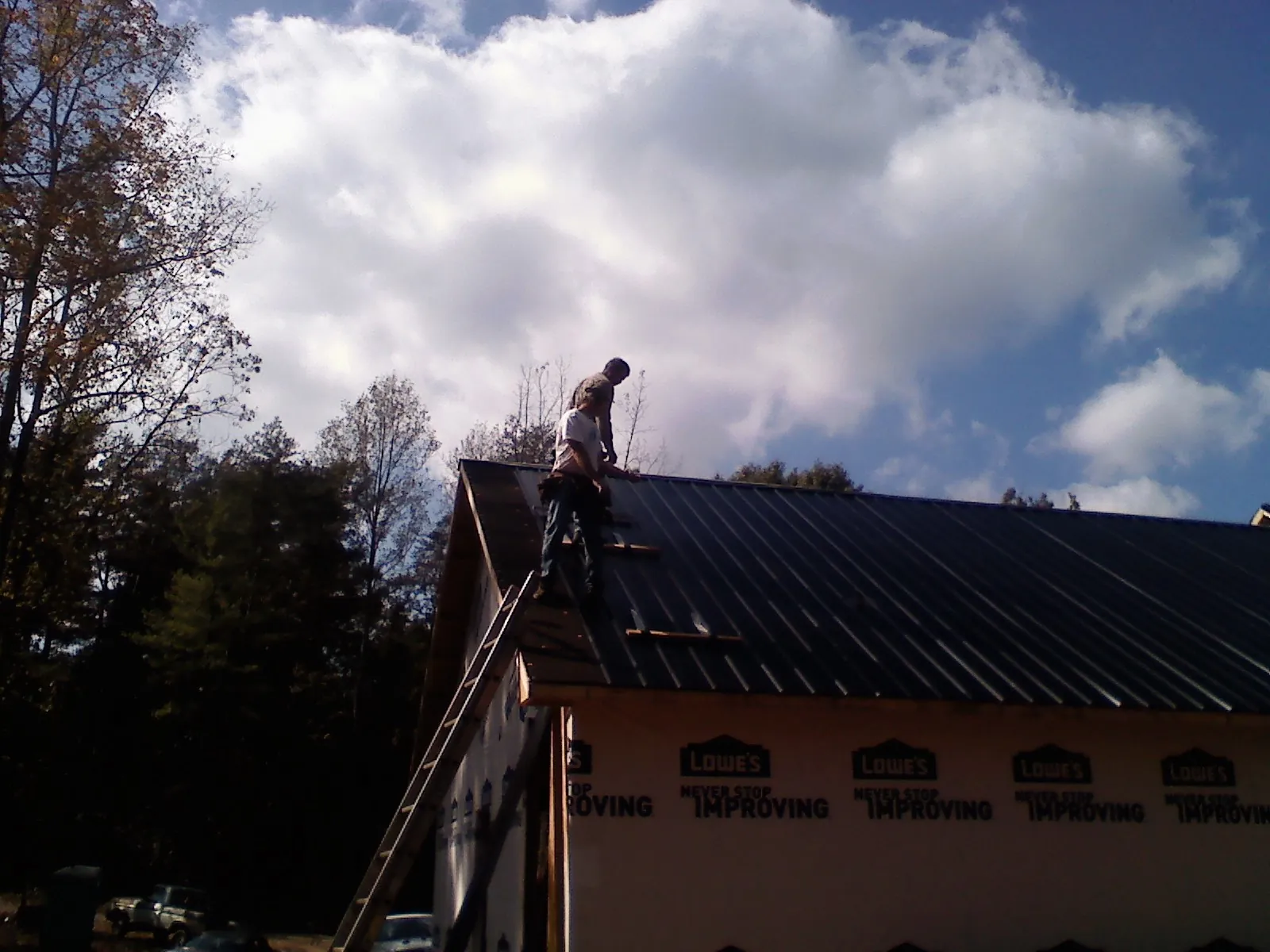Roofer fastening dark metal panels high against a cloudy sky, from a Roof Inspection job in Quogue