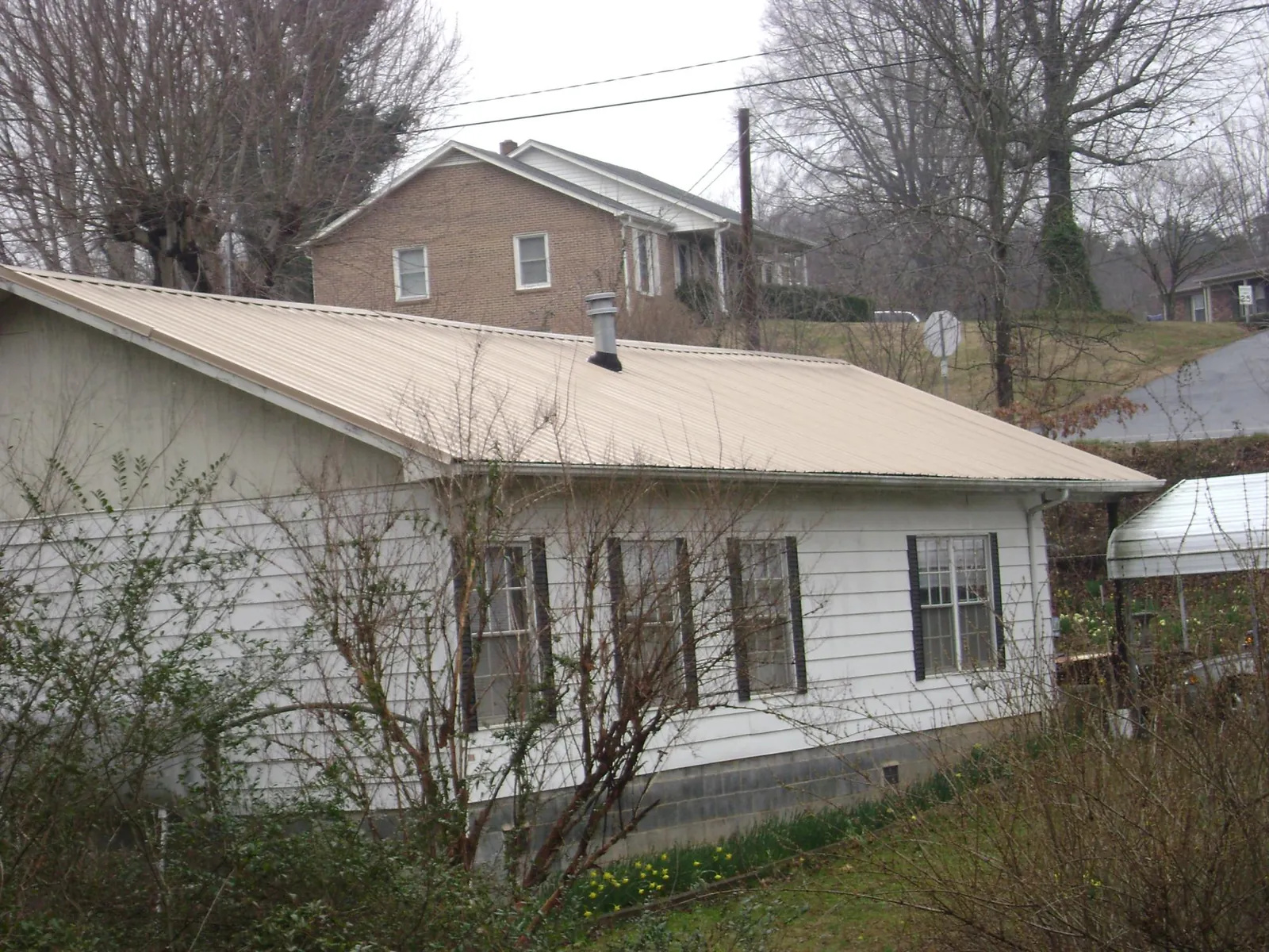 Tan metal roof on a white sided house set into a hillside — Commercial Roofing by Roofing Brothers in Quogue